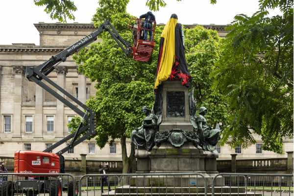 Mae'r artist Larry Achiampong yn goruchwylio lapio cerflun o William Gladstone mewn baner sy'n cynrychioli Affrica.